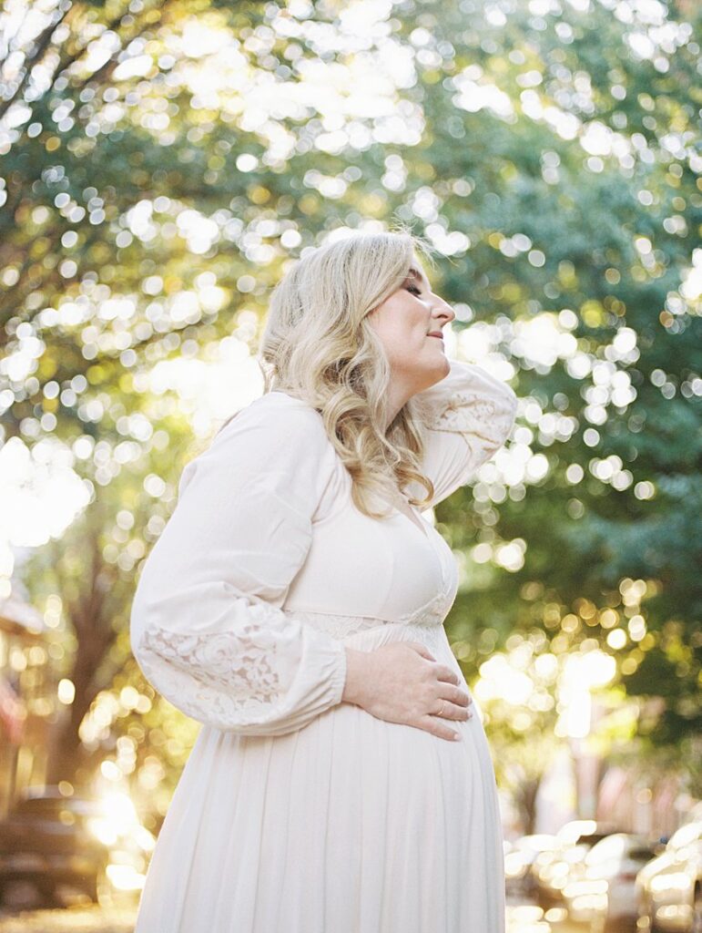 A Pregnant Mother Stands With One Hand On Her Belly And One Behind Her Head As She Gazes Up To The Sky - Maternity Photography In Alexandria Va By Marie Elizabeth Photography.