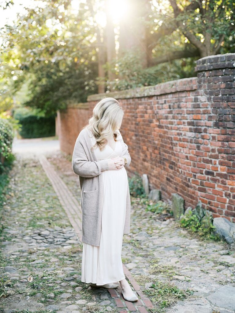 Blonde Expectant Mom Stands In An Alley In Old Town Alexandria Looking At Her Pregnant Belly.