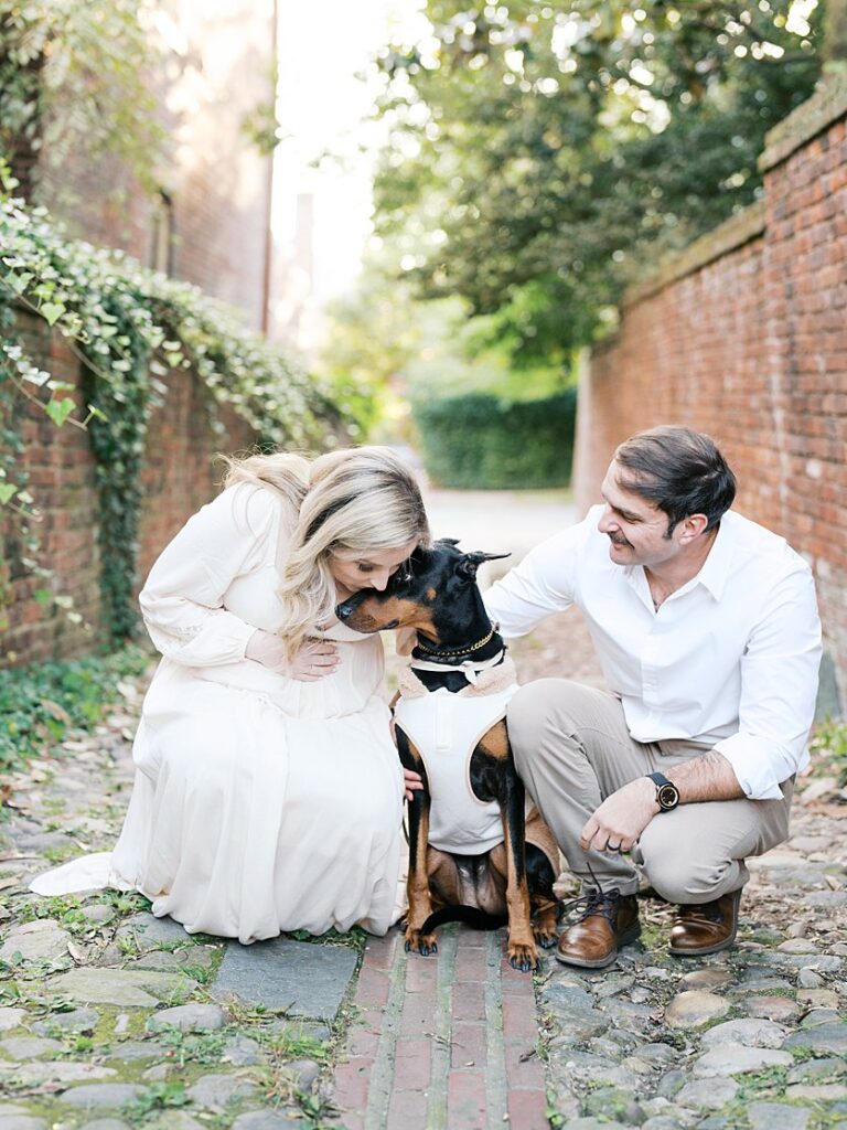 An Expecting Couple Kneel Down With Their Dog In An Alley In Old Town - Maternity Photography In Alexandria Va By Marie Elizabeth Photography.