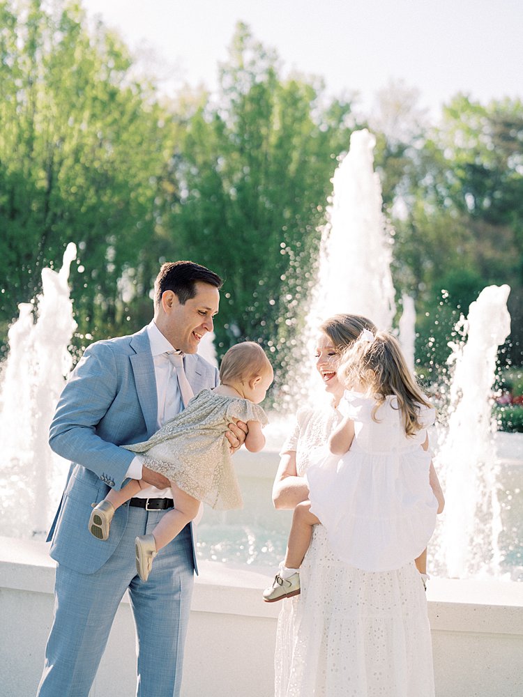 A Father Holds His Baby Girl Over To His Wife And Other Young Daughter During Their Mormon Temple Washington Dc Family Photos.