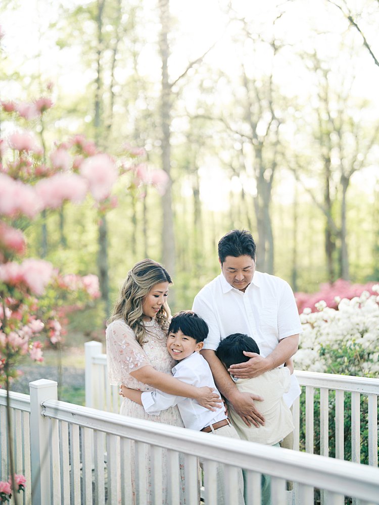 Family Of Four Stands On A Bridge Hugging In Brighton Dam Azalea Garden.
