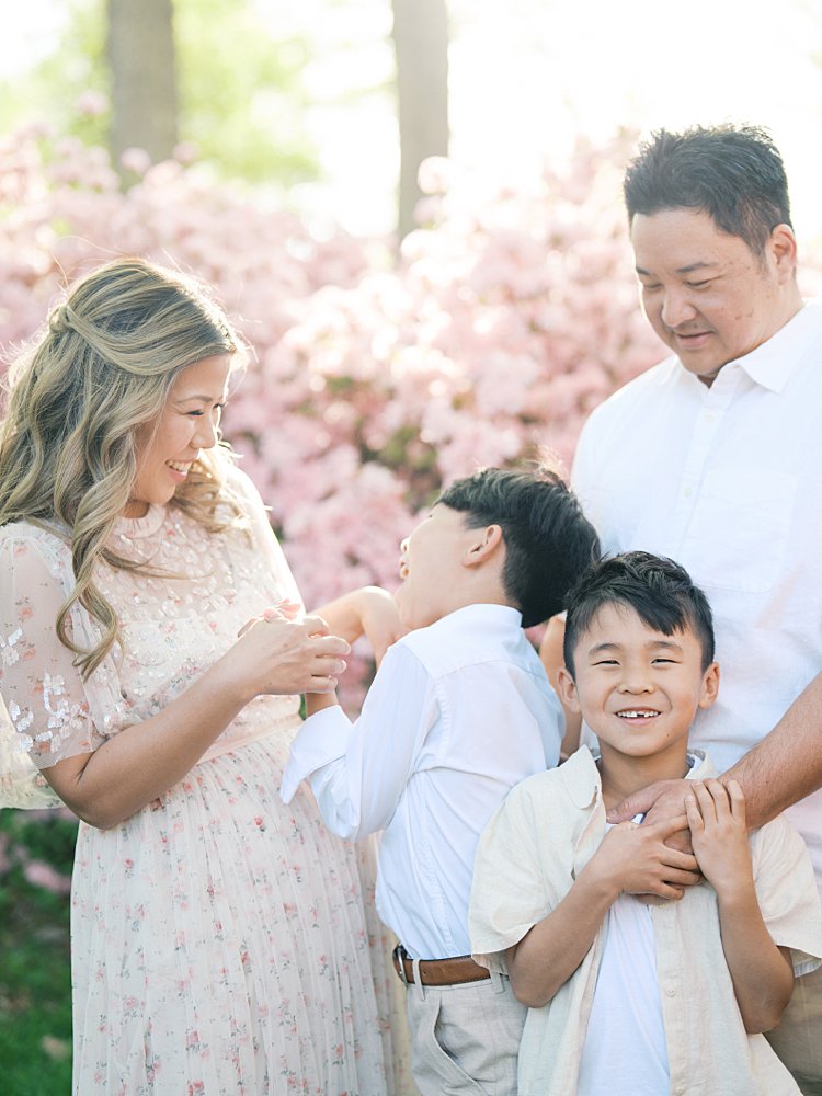 Family Of Four Tickles Each Other While Standing In Front Of Pink Azaleas.