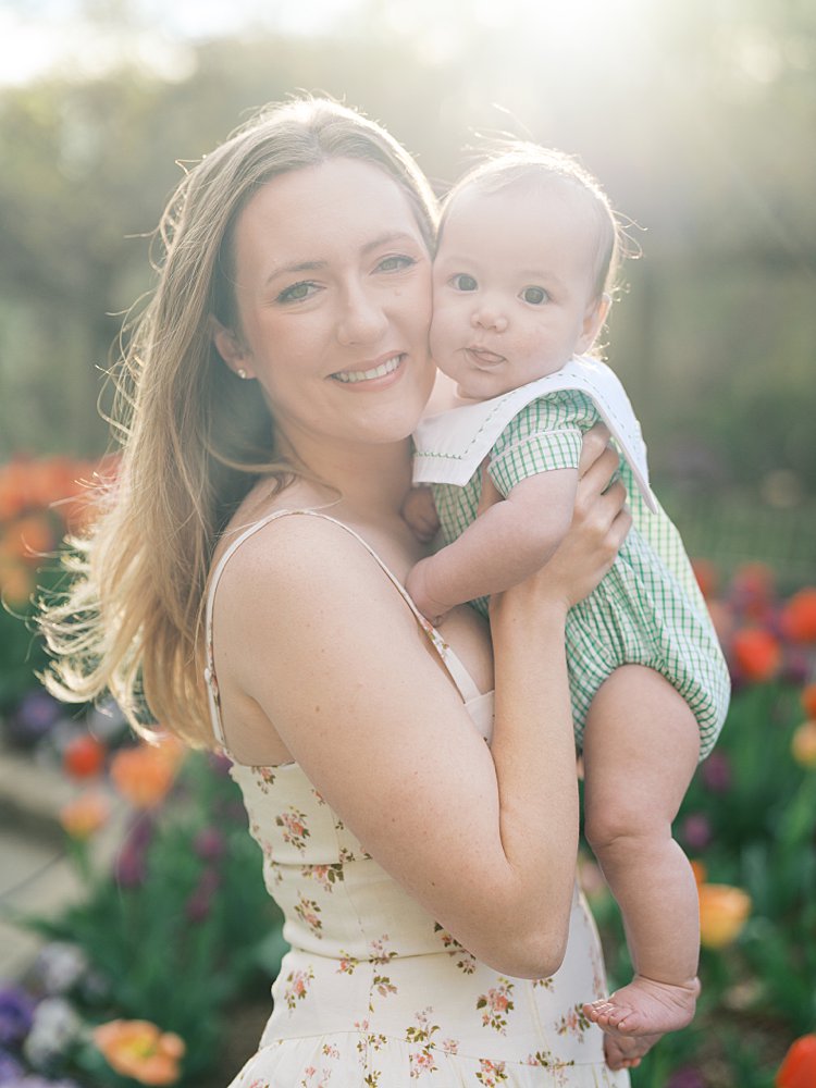 A Blonde Mother Holds Up Her Baby Boy And Smiles At The Camera.
