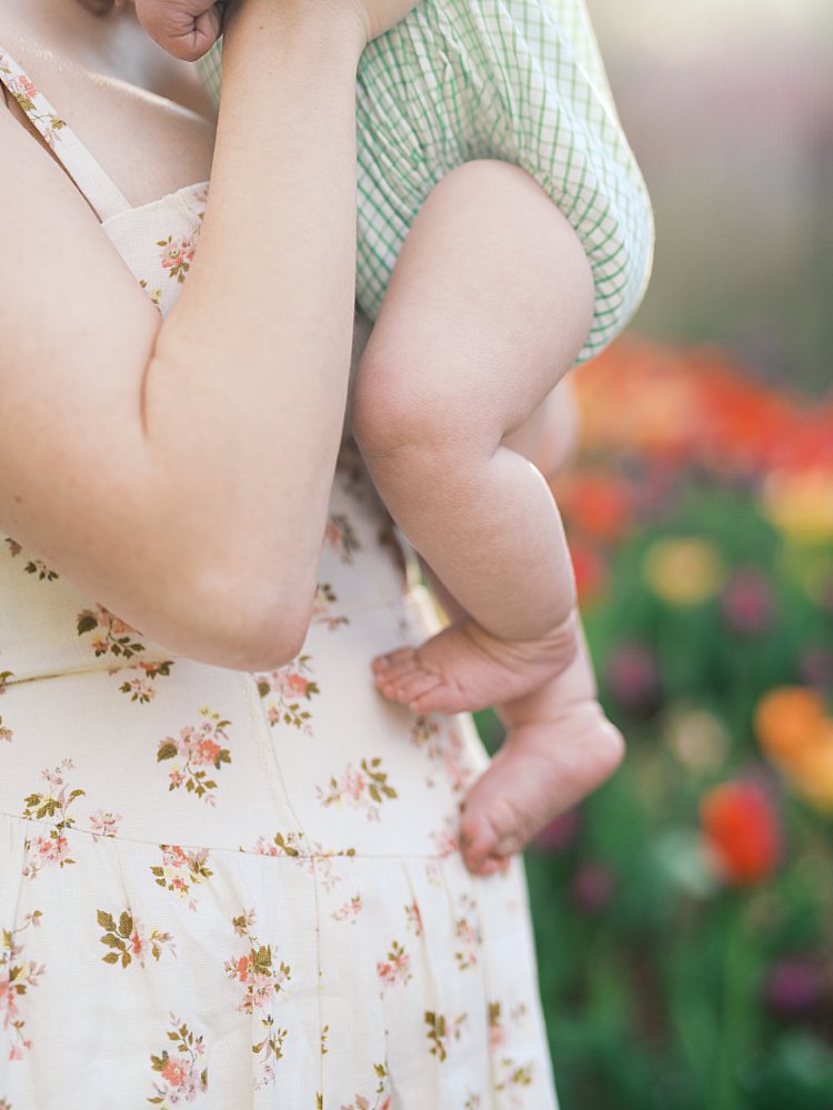 Close-Up View Of Baby Feet Being Held By A Mother In A Floral Dress.