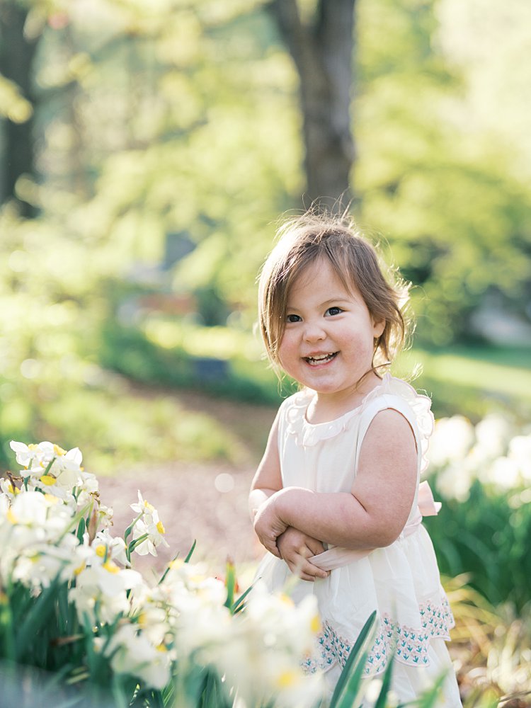 A Little Girl Gives A Big Smile As She Stands Near Some Daffodils. 
