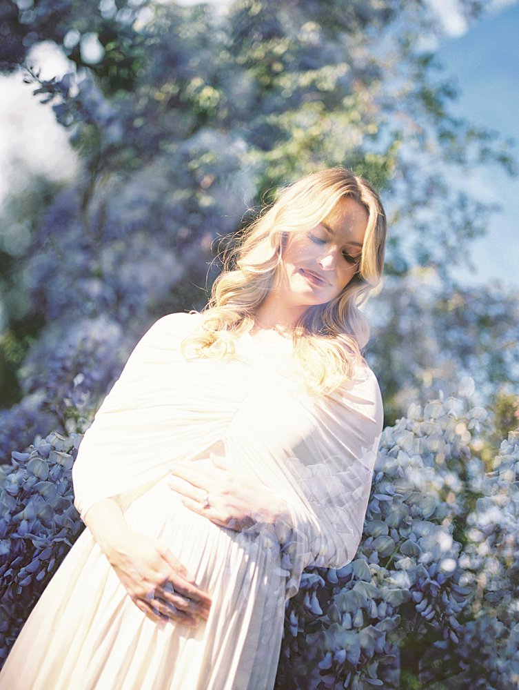 Double Exposure Of A Pregnant Mother With Blonde Hair Standing Against Wisteria.