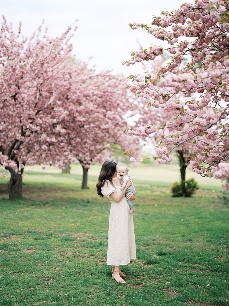 Mother With Long Brown Hair Holds Her Baby Boy At The Hains Point Cherry Blossoms.