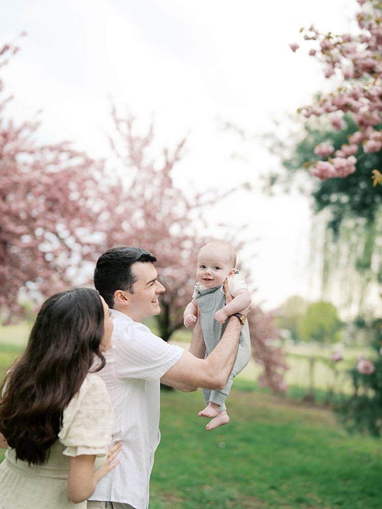 Baby Boy Is Held Up In The Air By His Parents During Their Family Photos.