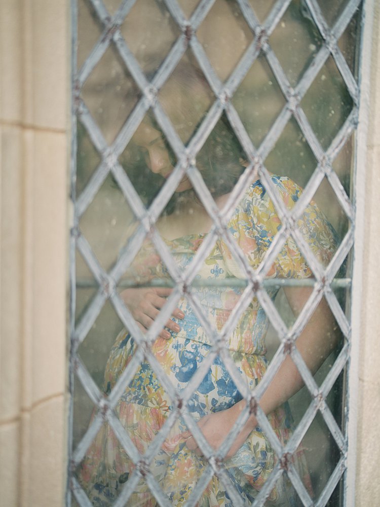 A Pregnant Woman Stands Behind A Stained Glass Window During Her National Cathedral Maternity Session.