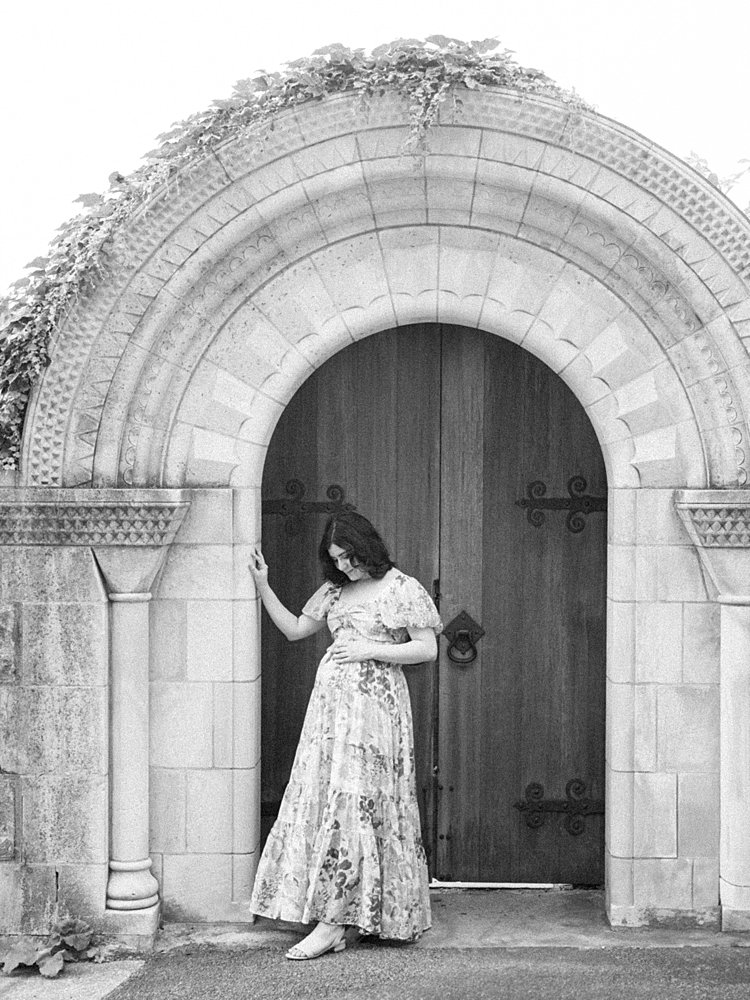 A Black And White Image Of A Mother Standing In An Archway At Bishop's Garden At The National Cathedral.