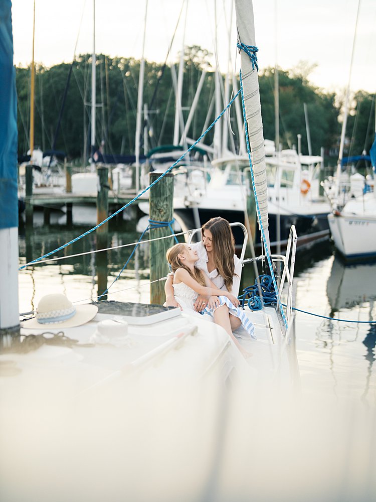Mother and daughter sit on the bow of a sailboat, photographed by Annapolis Family Photographer, Marie Elizabeth Photography.