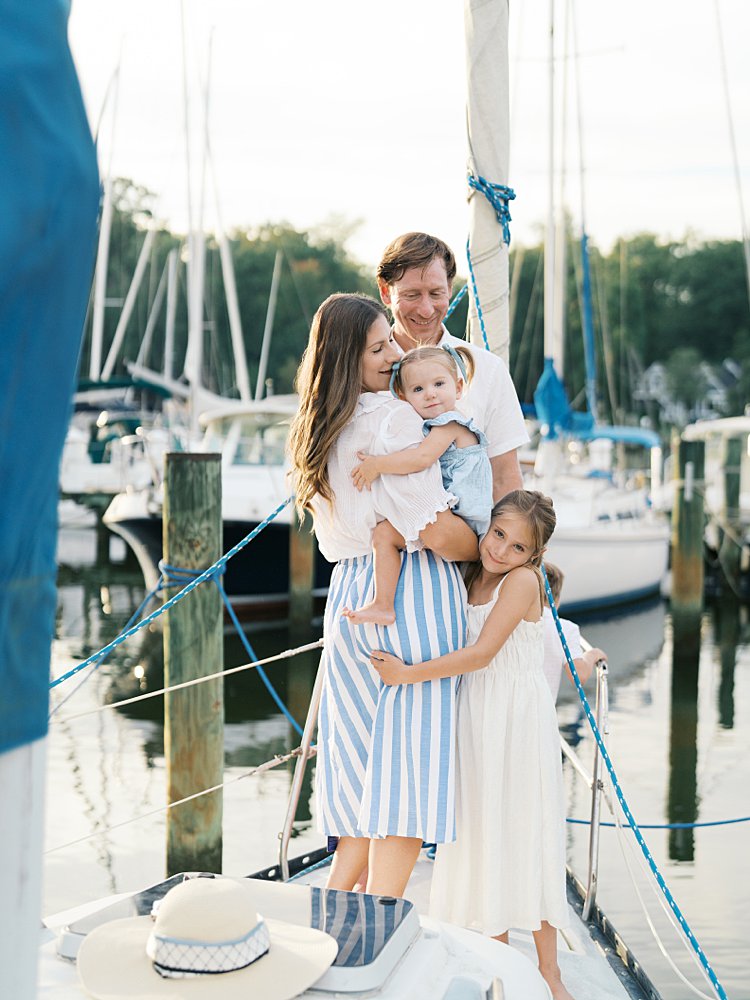 Family hug on a sailboat, consisting of mother, father, baby girl, and older sister.