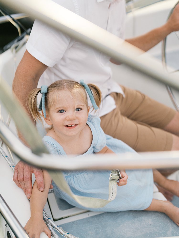 Little girl with pigtails with blue bows sit on a sailboat with her father.