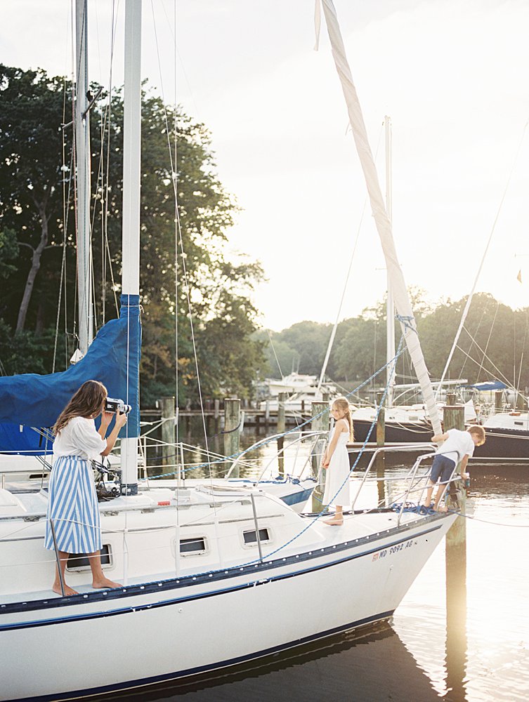 A mother uses a Super 8 film camera to film her two young children on a sailboat, photographed by Annapolis Family Photographer, Marie Elizabeth Photography.