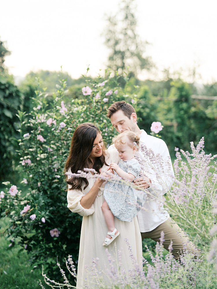 A mother and father hold their daughter as she looks as some purple flowers at Oatlands Historic Home and Gardens.