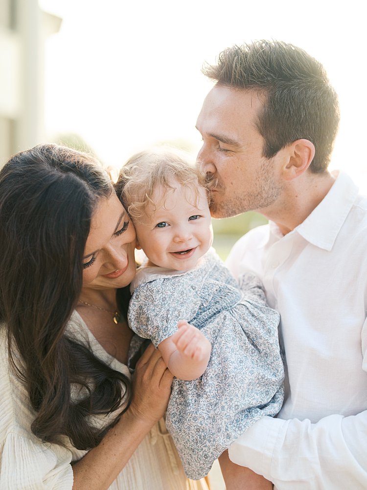 Oatlands VA family photos of a mother and father holding their daughter between them, kissing her and smiling.