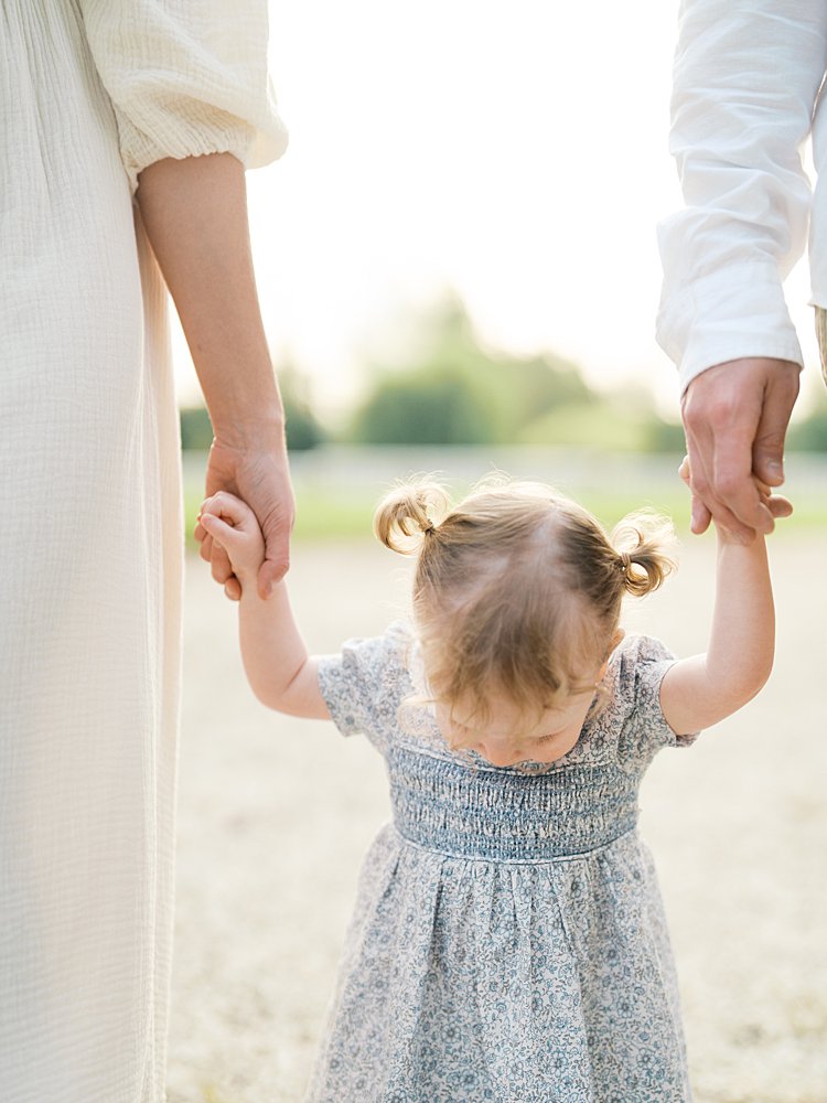 Oatlands VA family photos of a little girl with pigtails looking down as she holds her mother and father's hands.