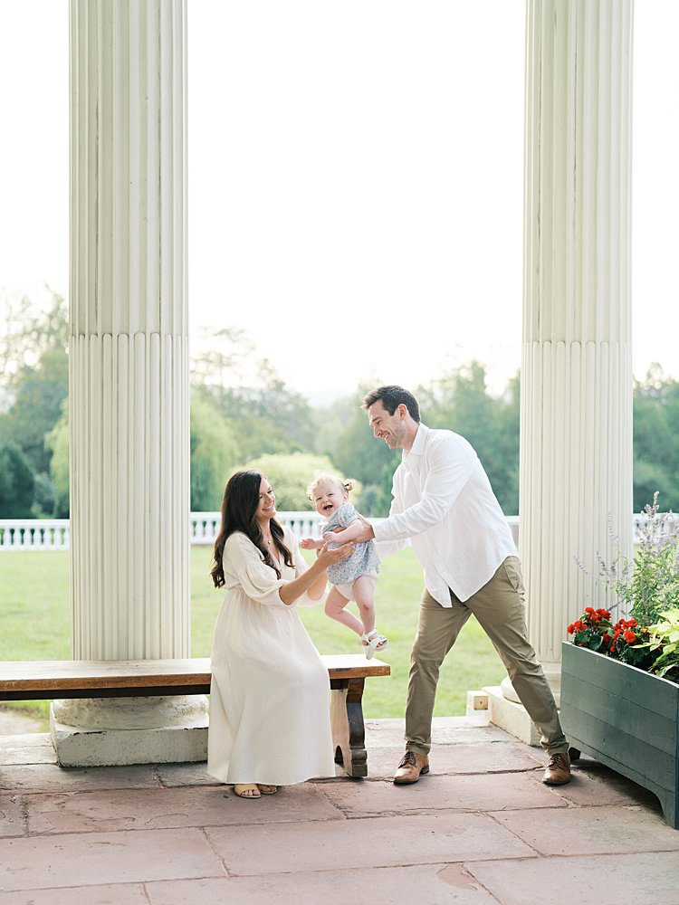 A father swings his toddler daughter towards her mother on the porch of Oatlands Historic Home in Oatlands, Virginia.