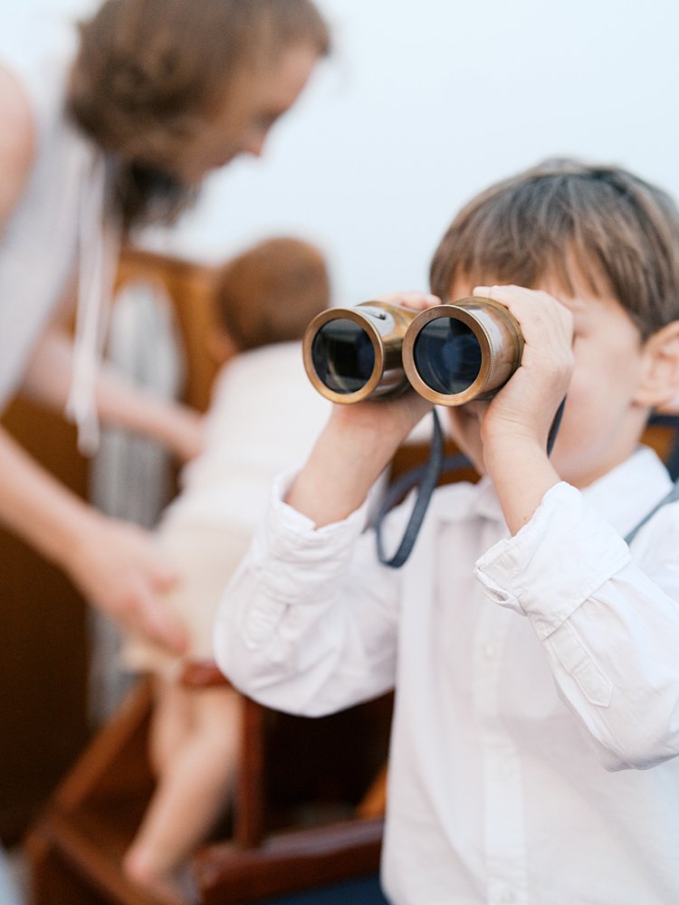 Little boy looks through binoculars while on a sailboat.