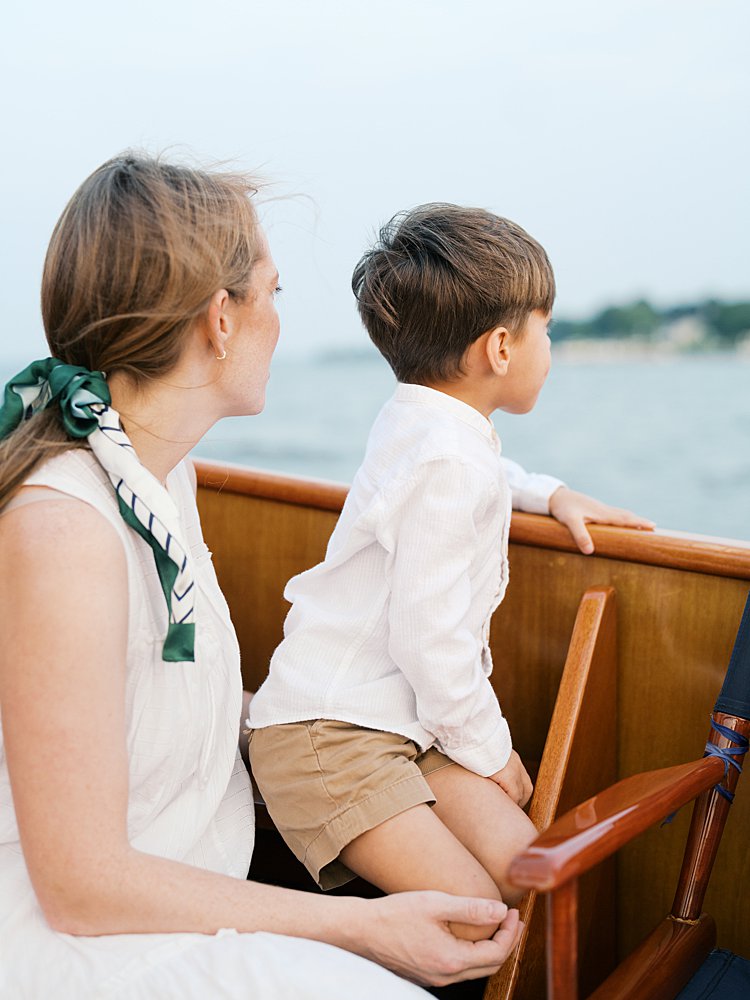 Mother sits on boat with her young son, looking out at the water.