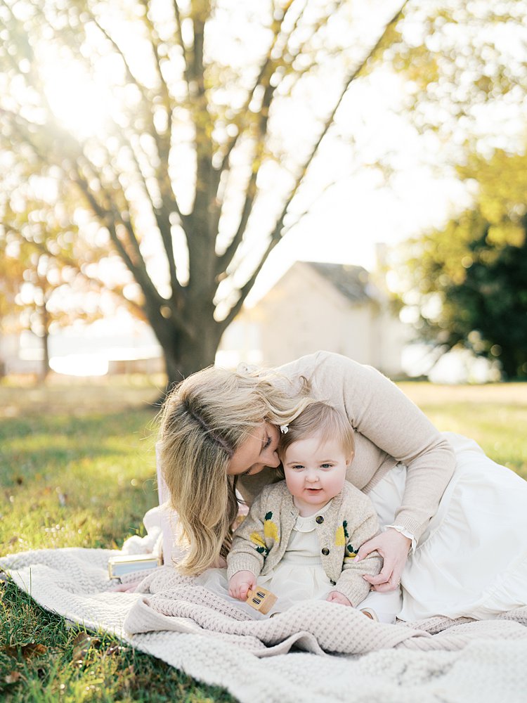A Mother Leans Down To Kiss The Side Of Her Daughter's Cheek During Their Jones Point Park Family Photos.