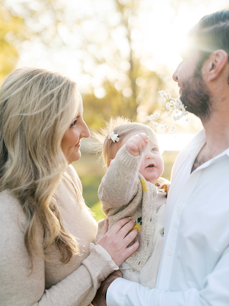 A Baby Girl Holds Up Some Baby's Breath Flowers To Her Father's Face During Their Jones Point Park Family Photos.