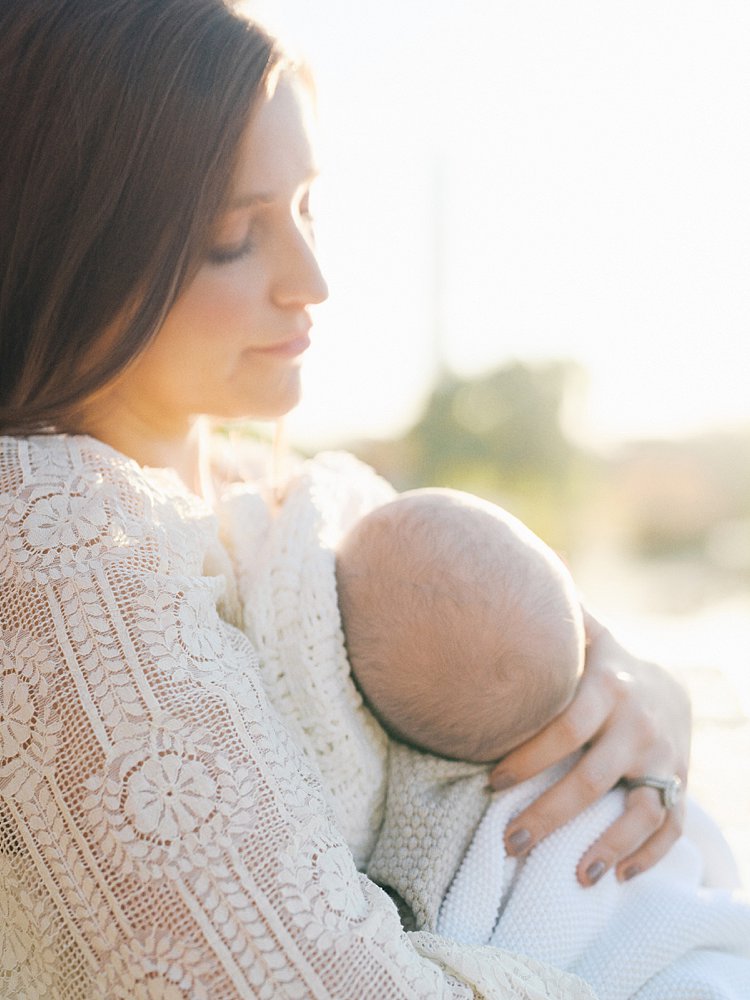 Mother Holds Baby Boy As He Sleeps With The Sun Glowing Behind Them.