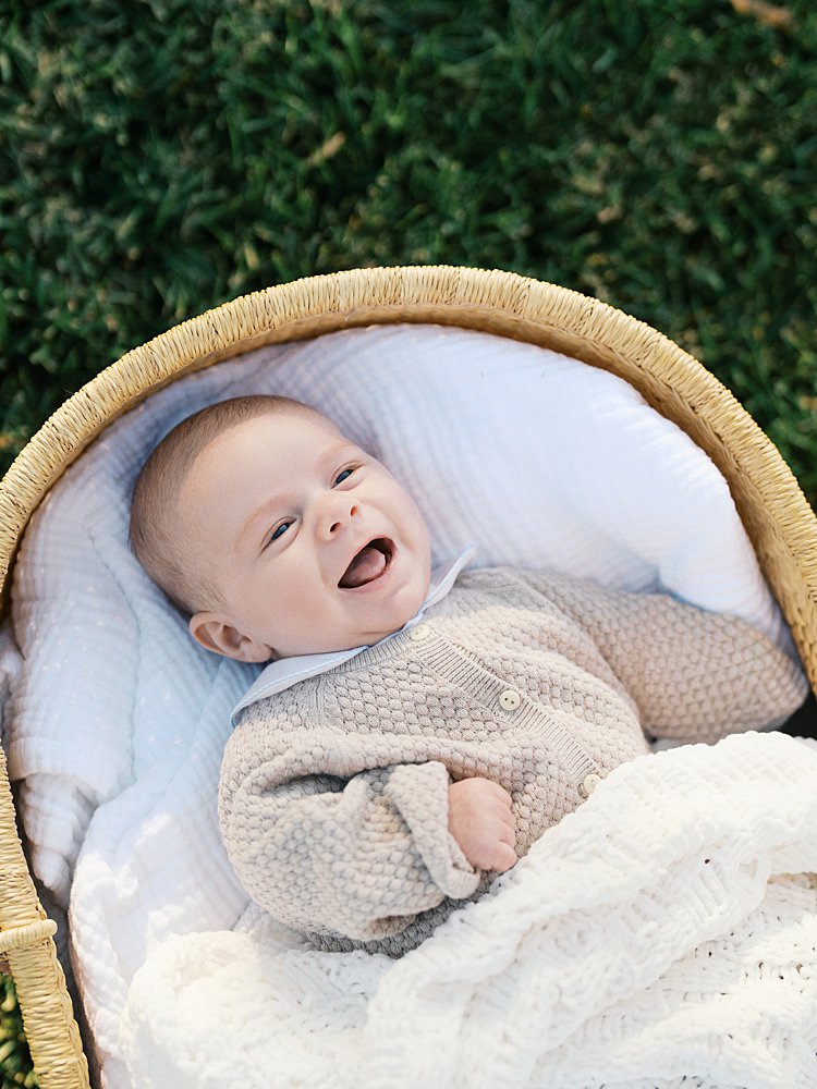 Baby Boy Smiles As He Lays In Moses Basket.
