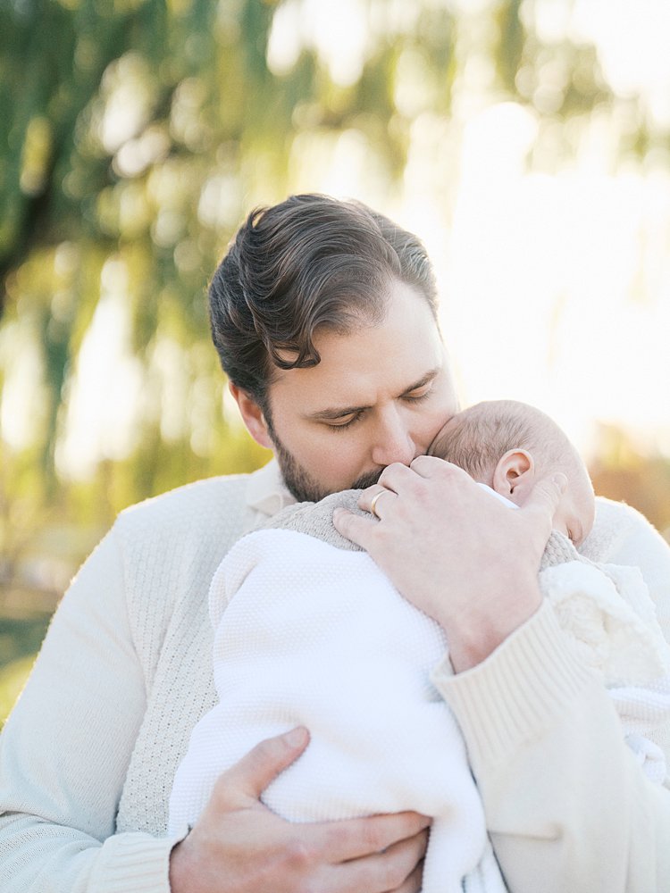 A Father Holds His Newborn Baby And Leans In To Kiss Him.