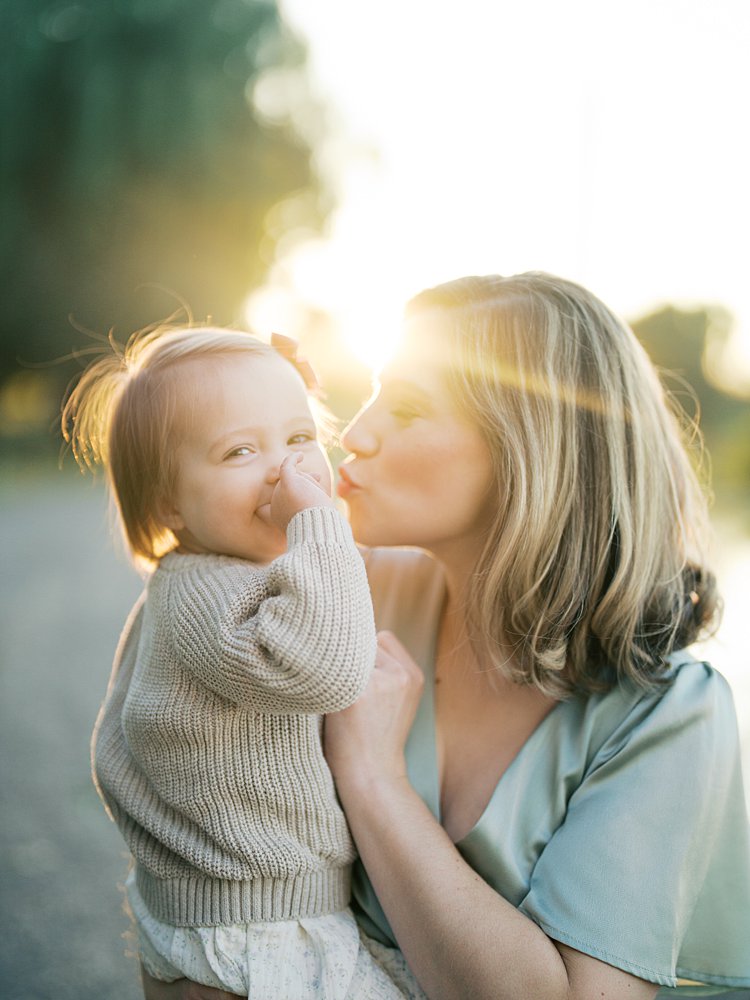 A Mother Kisses Her Baby Girl's Cheek As The Sun Shines Perfectly On Them During Their Downtown Dc Family Photos At Constitution Gardens.