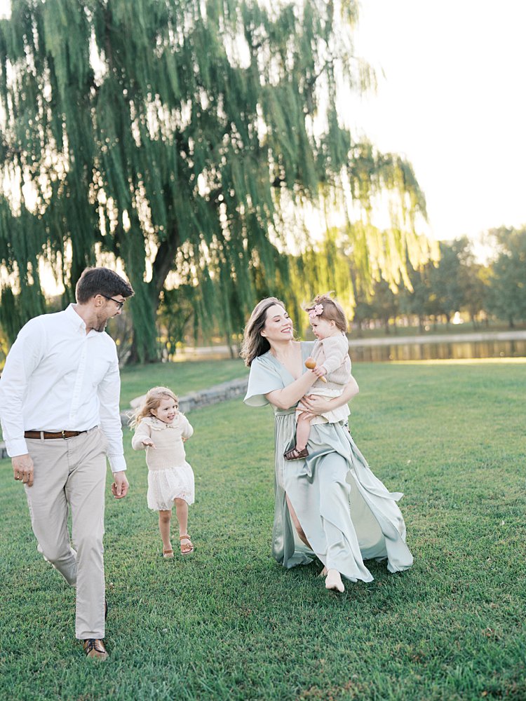 Family Of Four Run Together In Front Of A Big Green Willow Tree At Constitution Gardens In Washington, D.c.