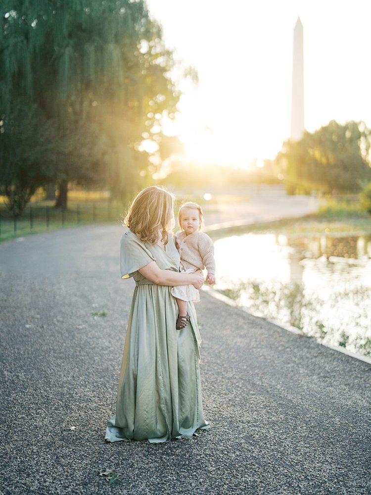 Mother In Green Satin Dress Stands Holding Her Baby Girl At Constitution Gardens.