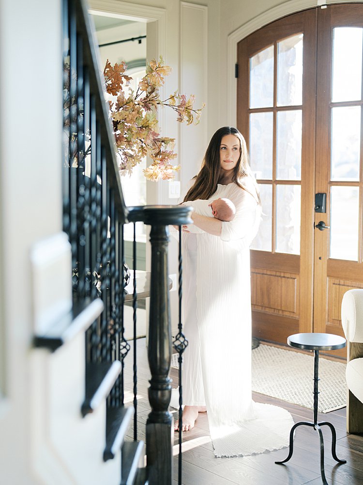 A Mother Stands In Her Entryway, Holding Her Newborn During Her Brookeville Md Newborn Photos.