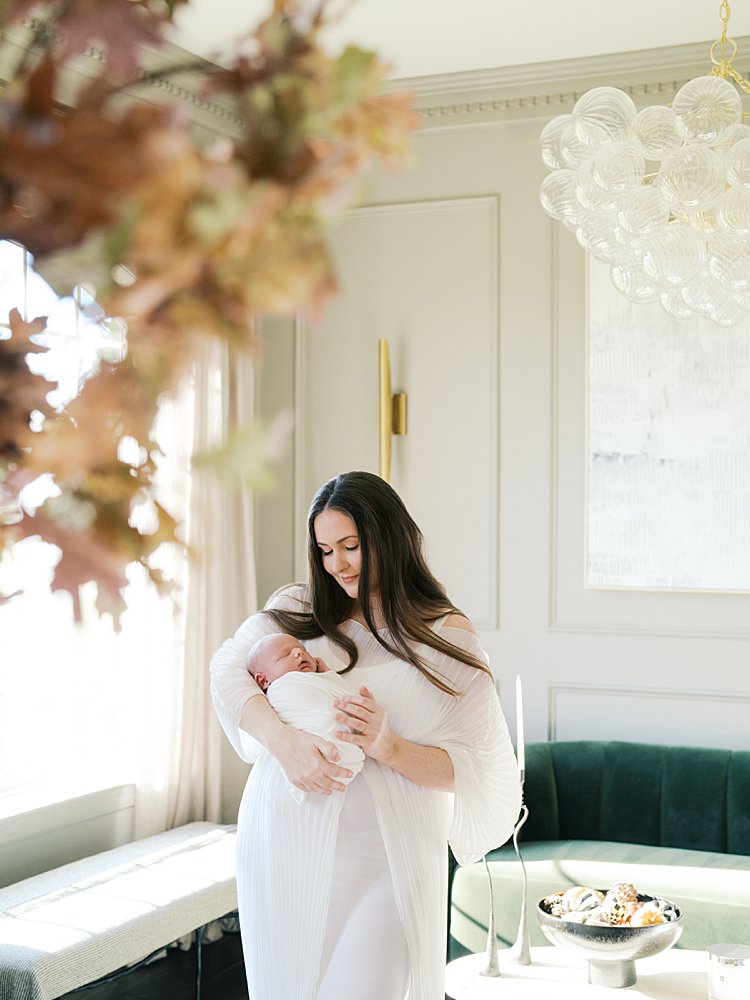 Mother With Long Brown Hair Smiles Lovingly Down At Her Newborn Son.