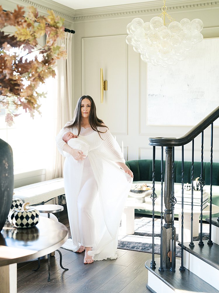 Mother In White Dress With Long Brown Hair Sways Her Dress Back And Forth While Holding Her Newborn During Their Brookeville Md Newborn Photos.