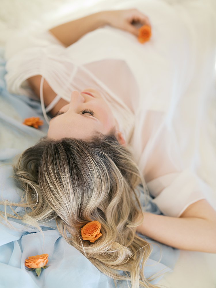 Blonde Woman Lays Down On Light Blue Fabric With Orange Flowers.