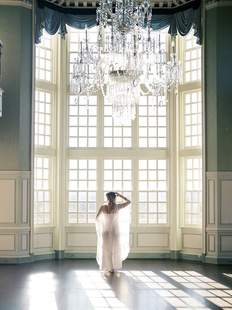 Pregnant Woman Stands In Front Of Large Window Area During Her Maternity Photos At The Estate At River Run.