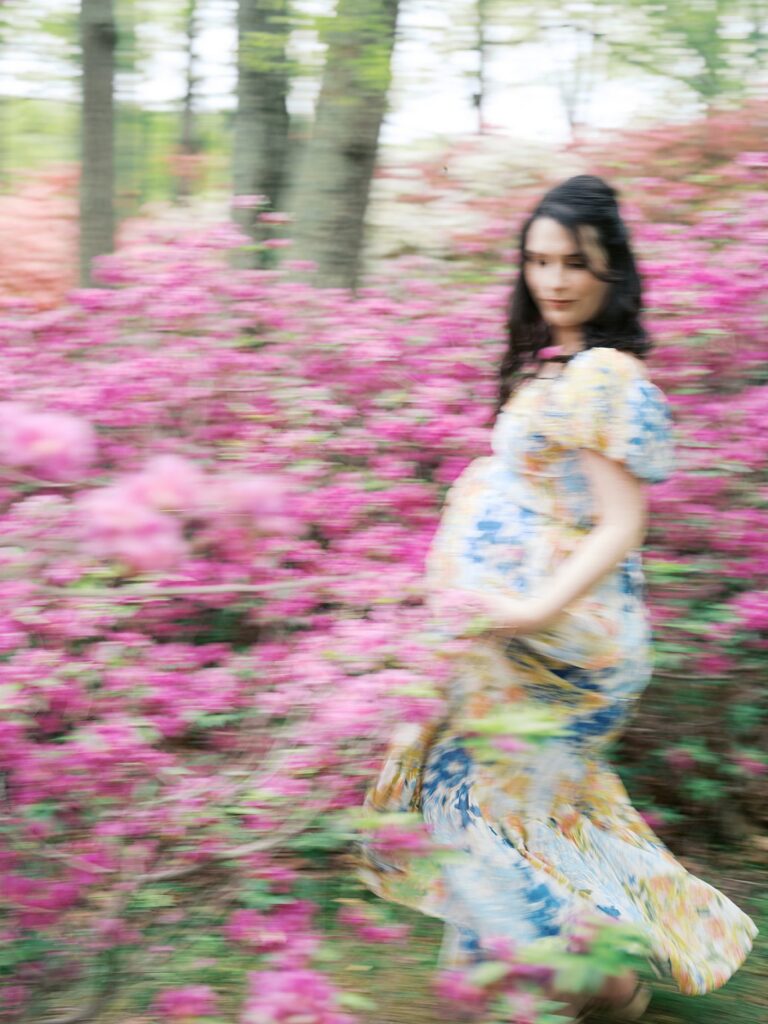 A Dreamy, Motion-Blur Image Of A Pregnant Woman Twirling Through A Field Of Hot Pink Azaleas At Brighton Dam, Her Floral Dress Swirling Around Her In One Of The Most Ethereal Clarksville Maternity Photos Moments From This Spring Session