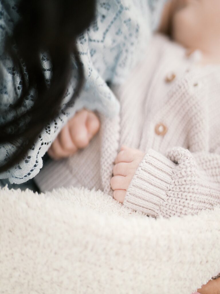 A Close-Up Detail Of A Newborn Baby Nestled Against A Mother's Chest, Wrapped In A Cream Knit Blanket With A Fluffy White Layer, Capturing The Tiny Details Of A Fresh New Baby