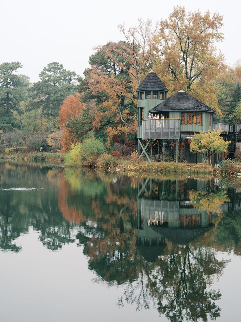 A Peaceful Lakeside View With A Treehouse Reflected In Still Water, Surrounded By Muted Autumn Tones And Soft Overcast Light.