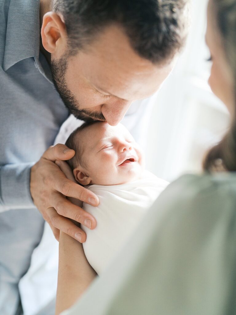 A Swaddled Newborn Rests Peacefully In Dad's Hands As Mom Looks On During A Newborn Photography Session In Washington Dc