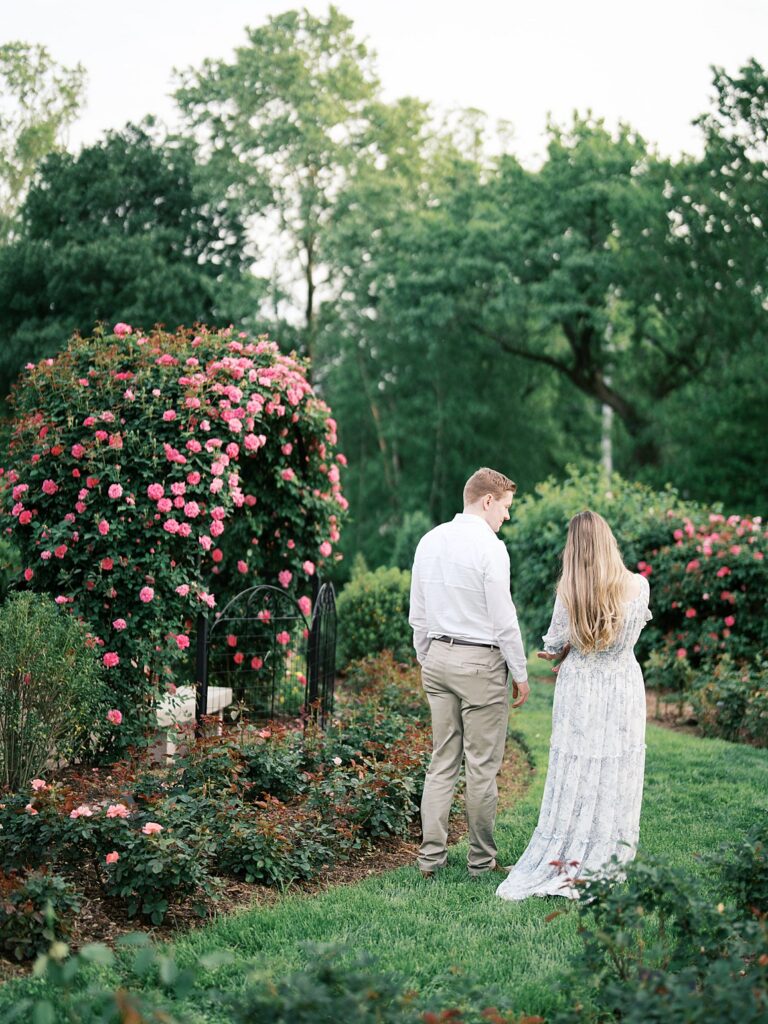 A Couple Walks Hand In Hand Through A Lush Rose Garden, Showing How Relaxed And Unhurried A Newborn Session Can Feel With A Washington Dc Newborn Photographer