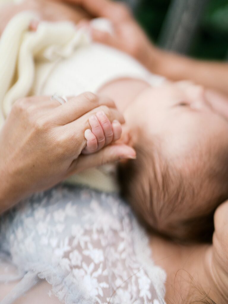 An Extreme Close-Up Of A Newborn Baby's Tiny Hand And Peaceful Face, Capturing The Delicate Details That Make The First Two Weeks The Ideal Answer To How Old Should My Baby Be For Newborn Photos.