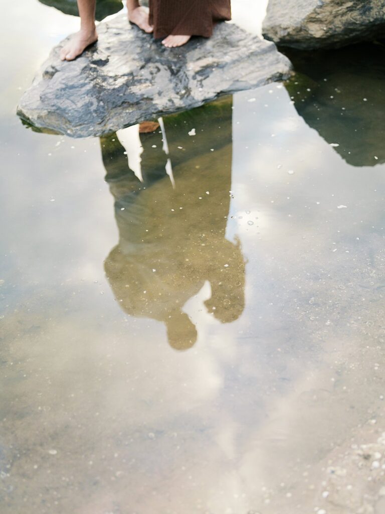 Artistic Reflection Portrait Of A Couple And Child Mirrored In Still Water Beside Natural Rock Formations, Creating A Dreamy And Emotional Family Image.