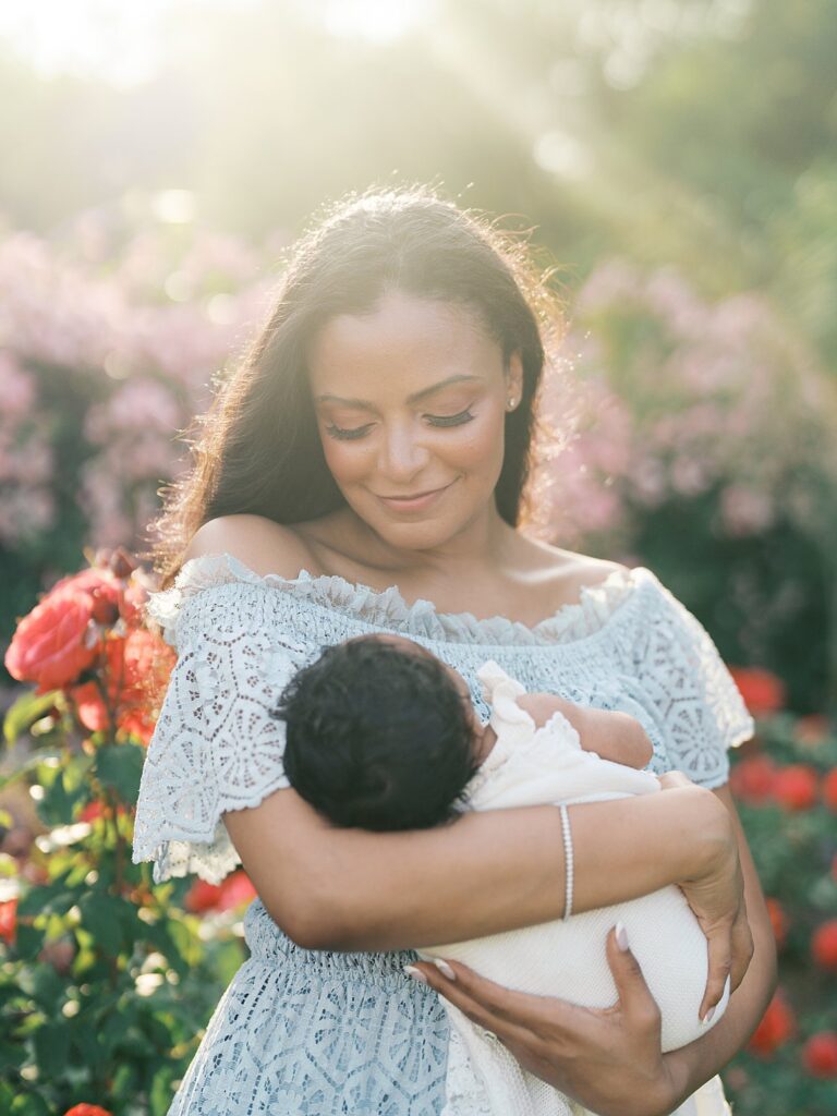 Mother Holding Her Newborn Daughter In A Blooming Garden At Sunset, Creating Romantic And Ethereal Family Portraits Filled With Soft Pastel Colors.