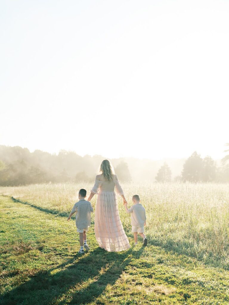 Mother Walking Hand In Hand With Her Two Young Sons Through A Sunlit Field, Captured By A Gainesville Photographer Near Gainesville, Va
