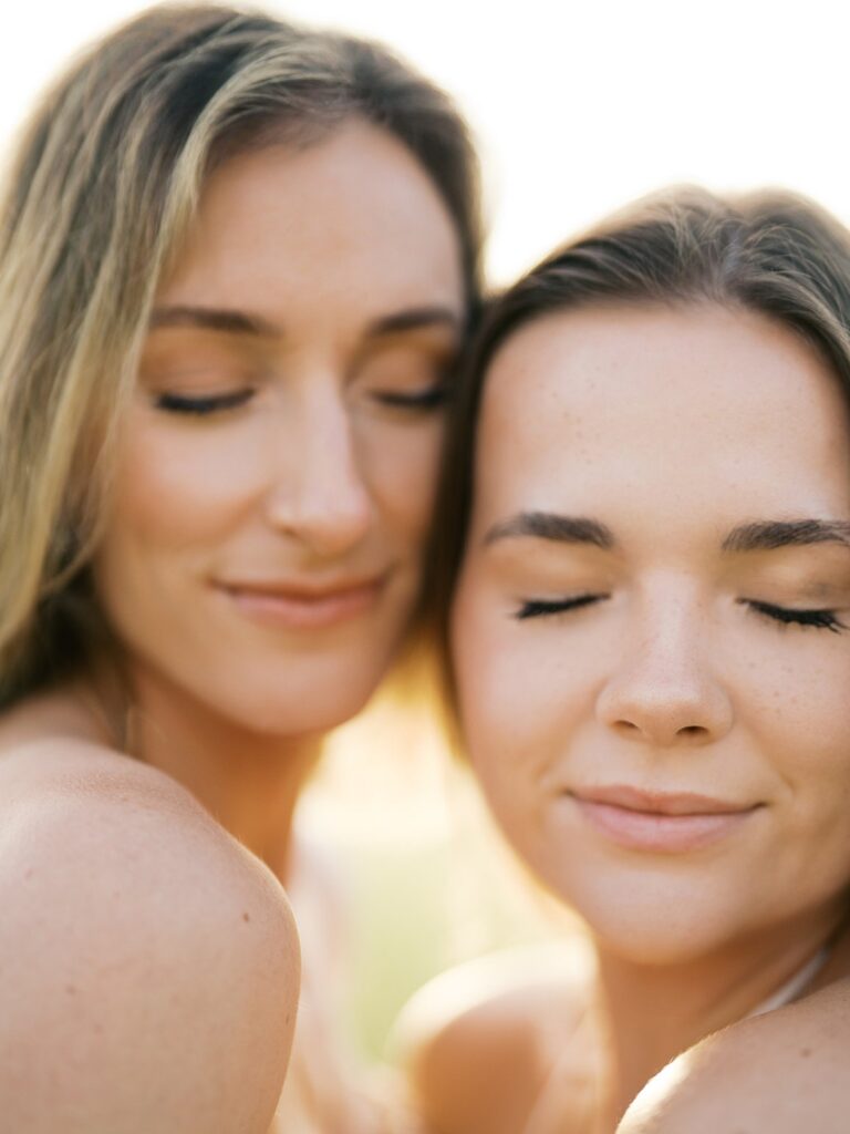 Close-Up Of Two Young Women Cheek To Cheek With Eyes Closed, Bathed In Warm Sunrise Light