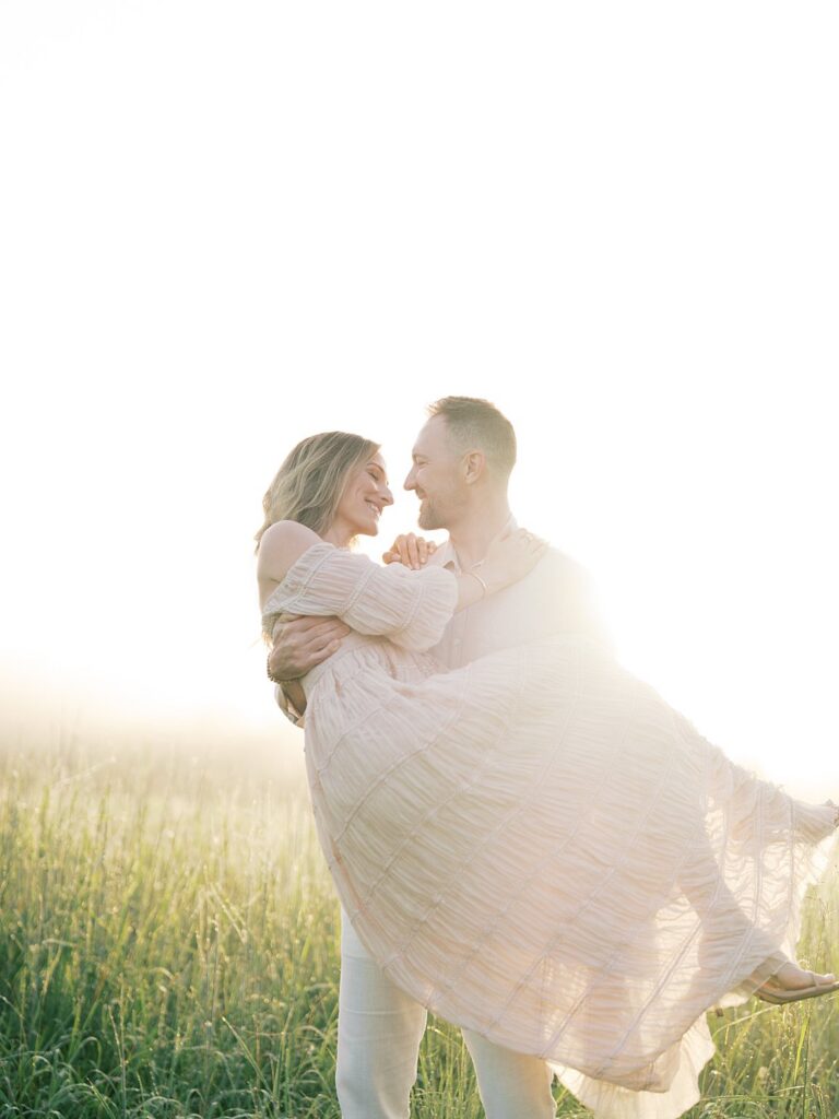 Husband Lifting His Wife In A Sun-Drenched Field During A Golden Hour Family Session Captured By A Gainesville Photographer