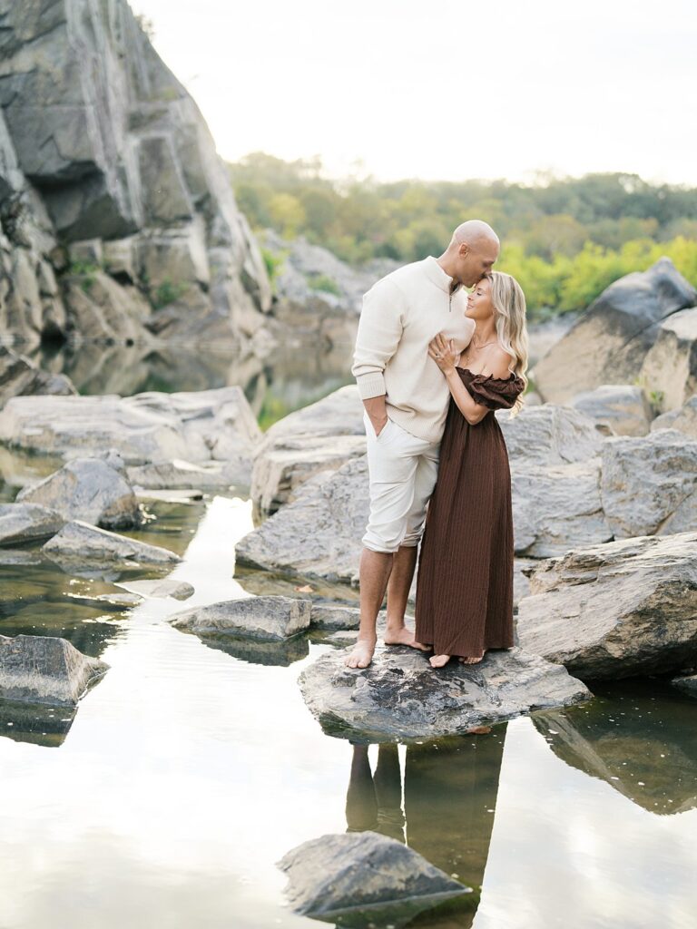 Couple Stands Barefoot On The Rocks Above The Calm Potomac At Great Falls, One Of The Most Scenic Washington Dc Fall Foliage Locations For A Session.
