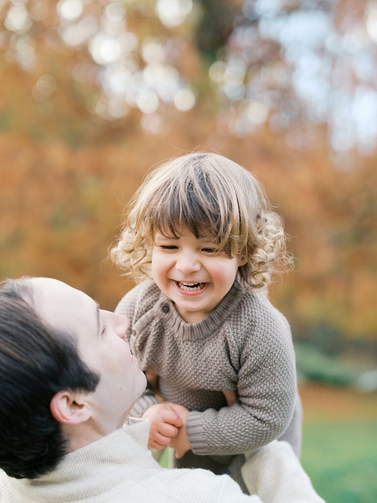 Father Laughs With His Giggling Son Against A Soft Autumn Backdrop At Brookside Gardens, A Favorite Among Washington Dc Fall Foliage Locations.